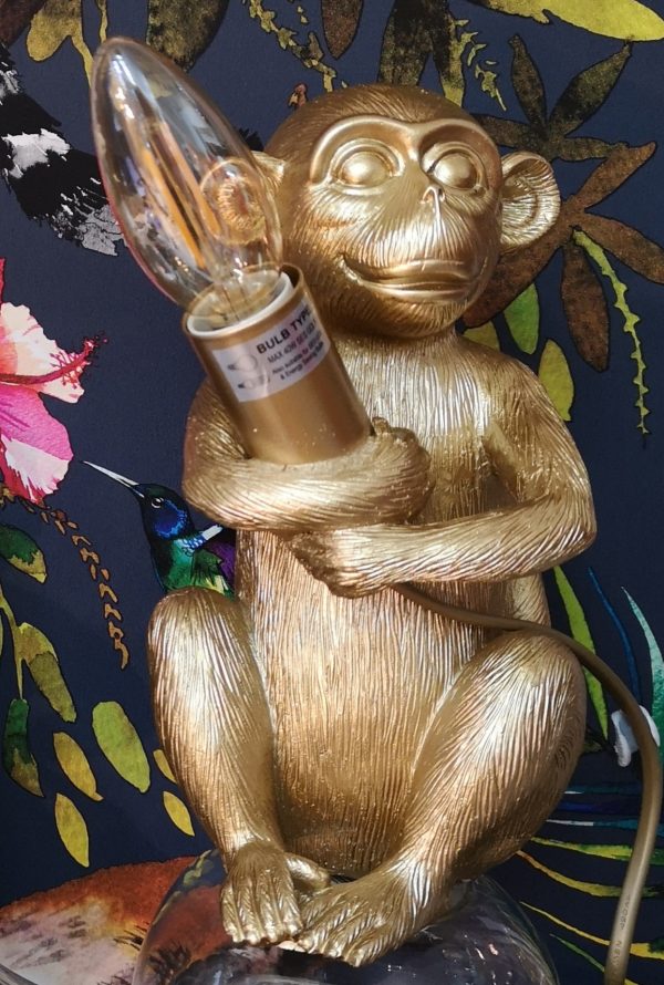 A gold table lamp of a monkey holding a LED candle bulb
