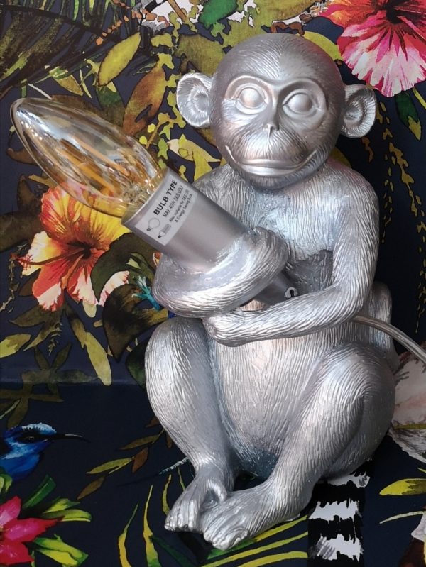 A silver table lamp of a monkey holding a LED candle bulb