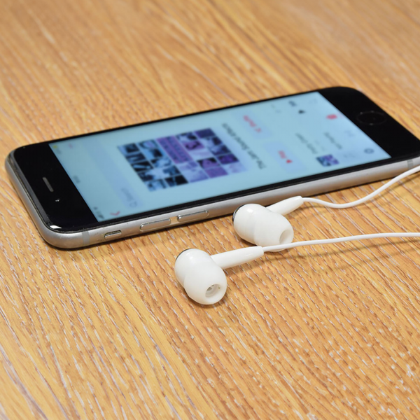 White Stereo Earphones with 3.5mm Stereo Jack plug next to a mobile phone on a table